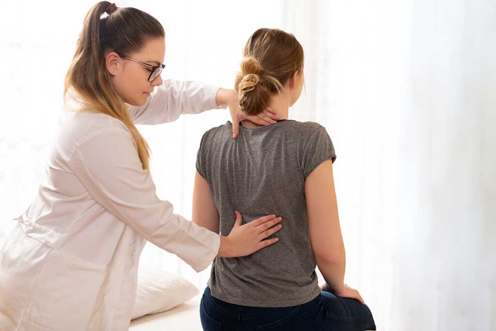 A person placing an ice pack on their lower back while seated on a living room couch.