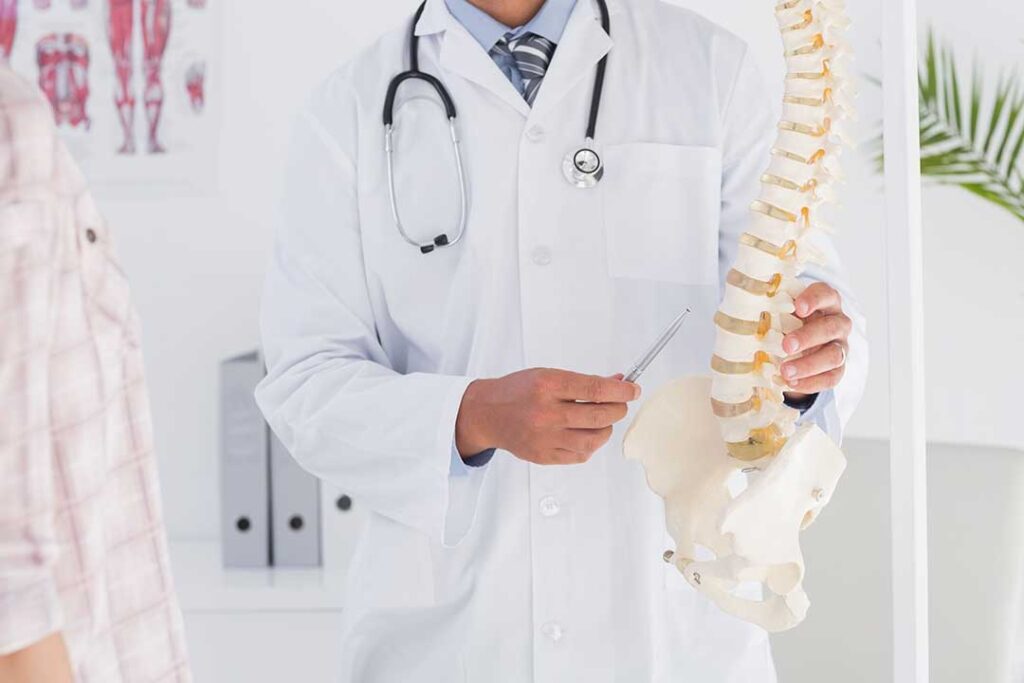 Chiropractic safety discussion with a patient reviewing symptoms beside an examination table.